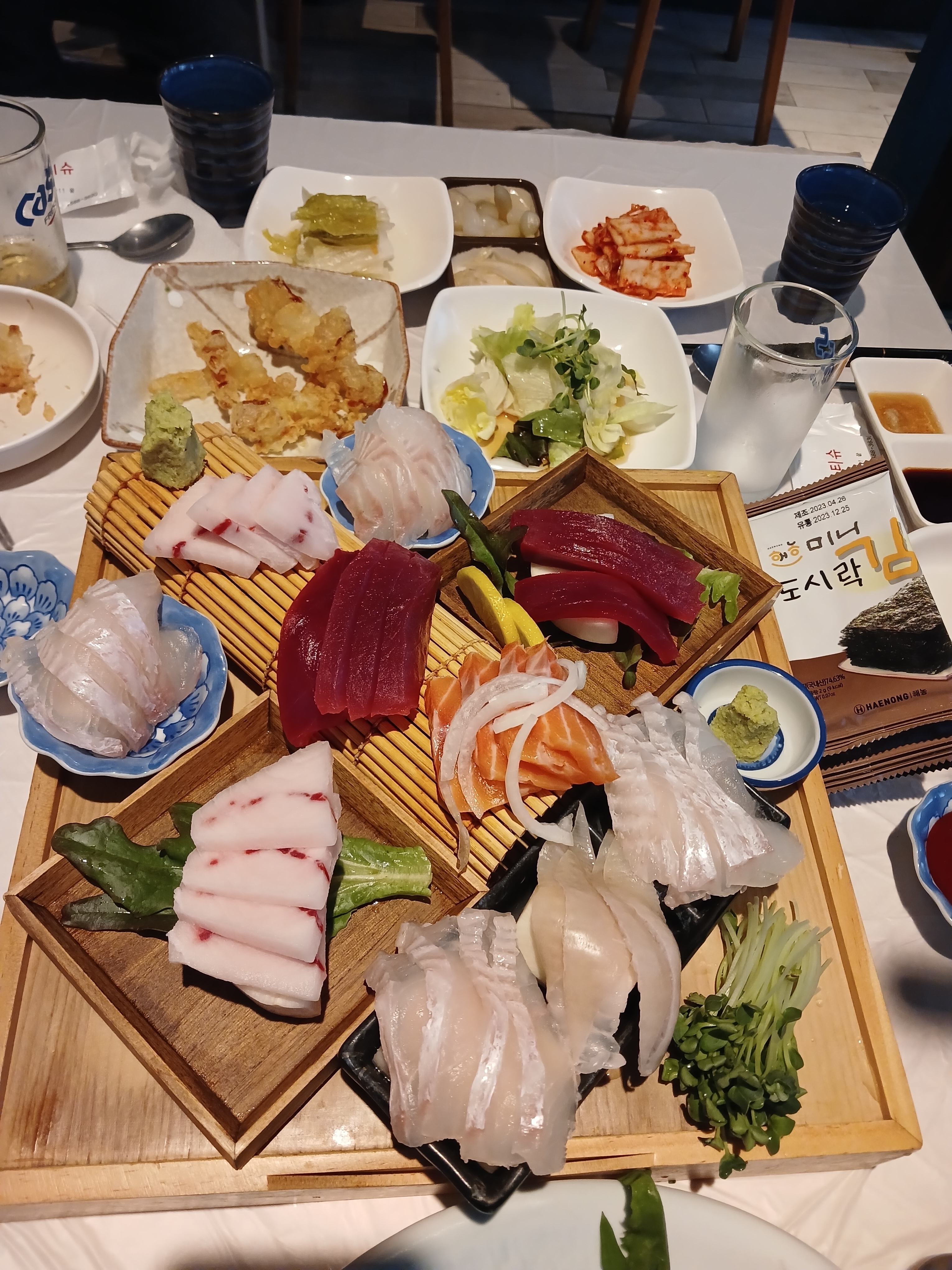 먹음직스러운 초밥이 나무 접시에 플레이팅되어 있고, 곁들임 채소가 보인다.