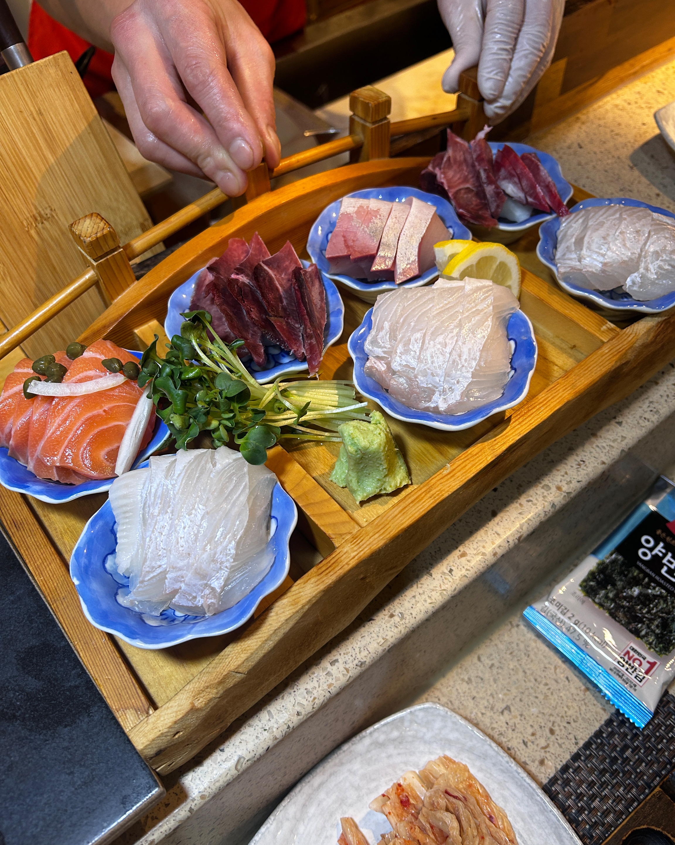 나무 접시에 다양한 종류의 초밥과 곁들임 채소가 보기 좋게 담겨 있다.