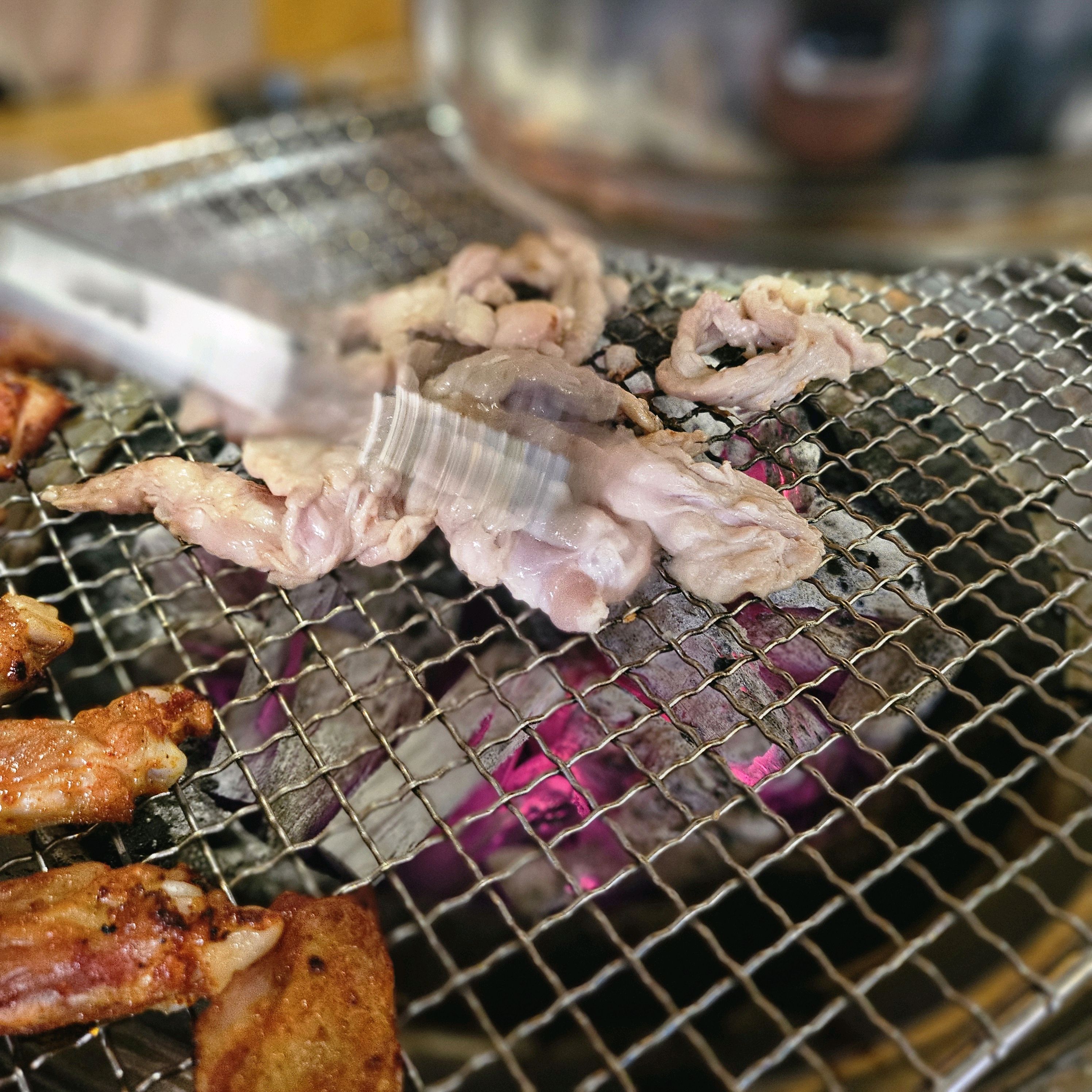 집게로 닭목살을 숯불 위에서 뒤집는 모습