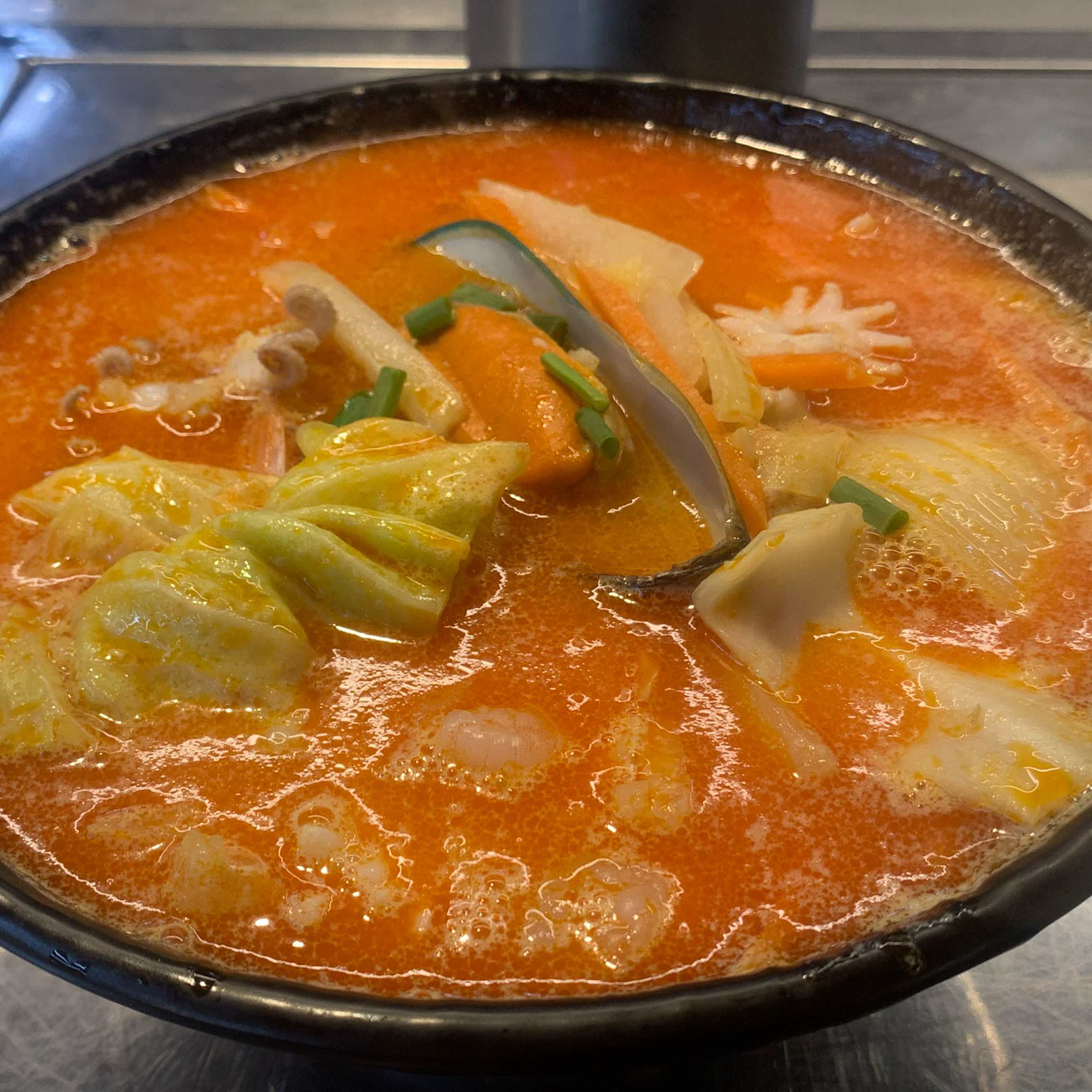 조개와 오징어, 채소가 붉은 국물에 담긴 해산물 쌀국수