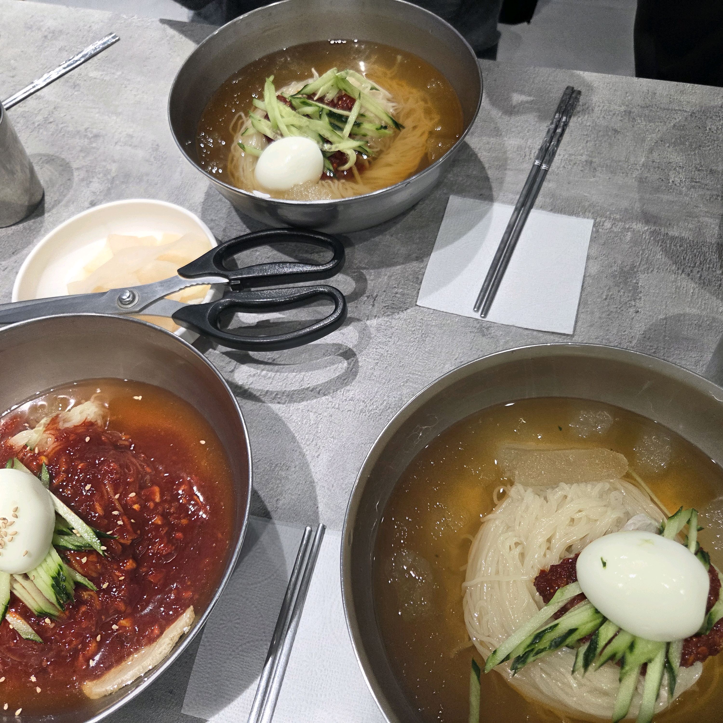 여러 사람이 함께 식사하는 모습. 테이블에는 다양한 밀면 메뉴가 놓여 있습니다.