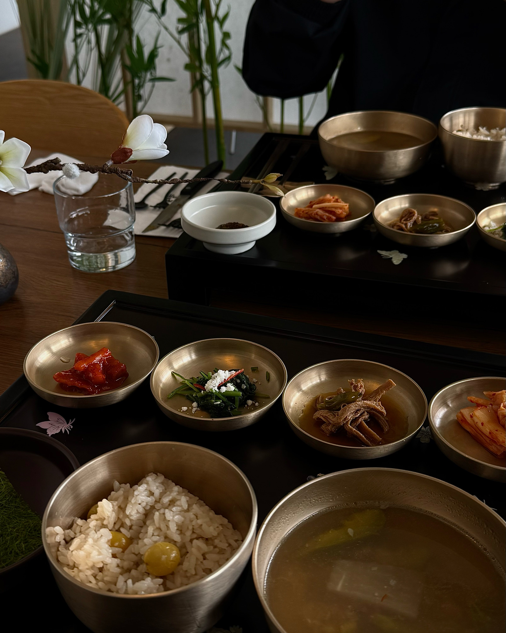 테이블 위에 놓인 놋그릇에 담긴 밥과 국, 그리고 여러 가지 반찬들. 옅은 갈색 테이블보 위로 정갈하게 배치되어 있다.