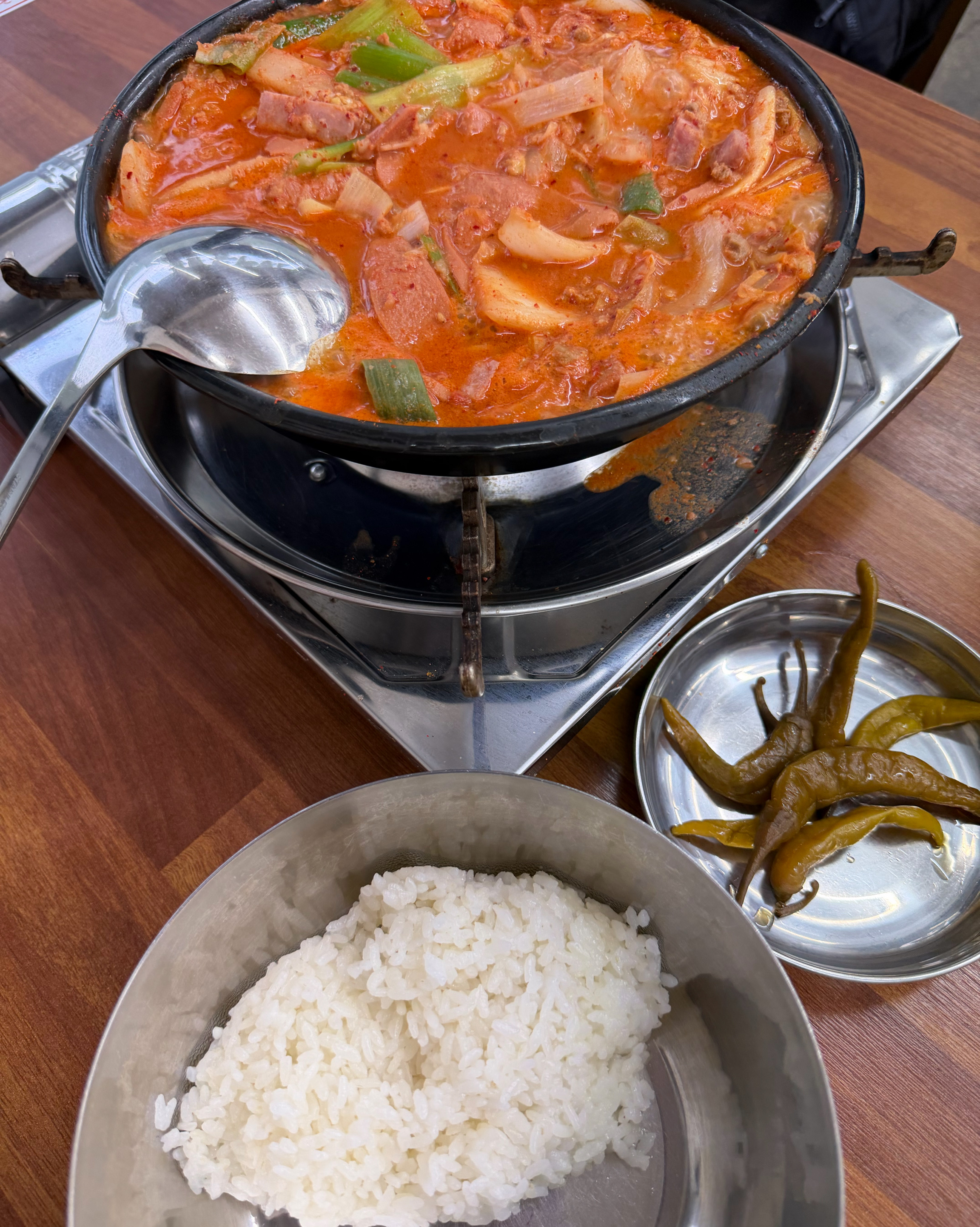 철제 냄비에 담긴 부대찌개와 밥 한 그릇, 그리고 곁들임 반찬.
