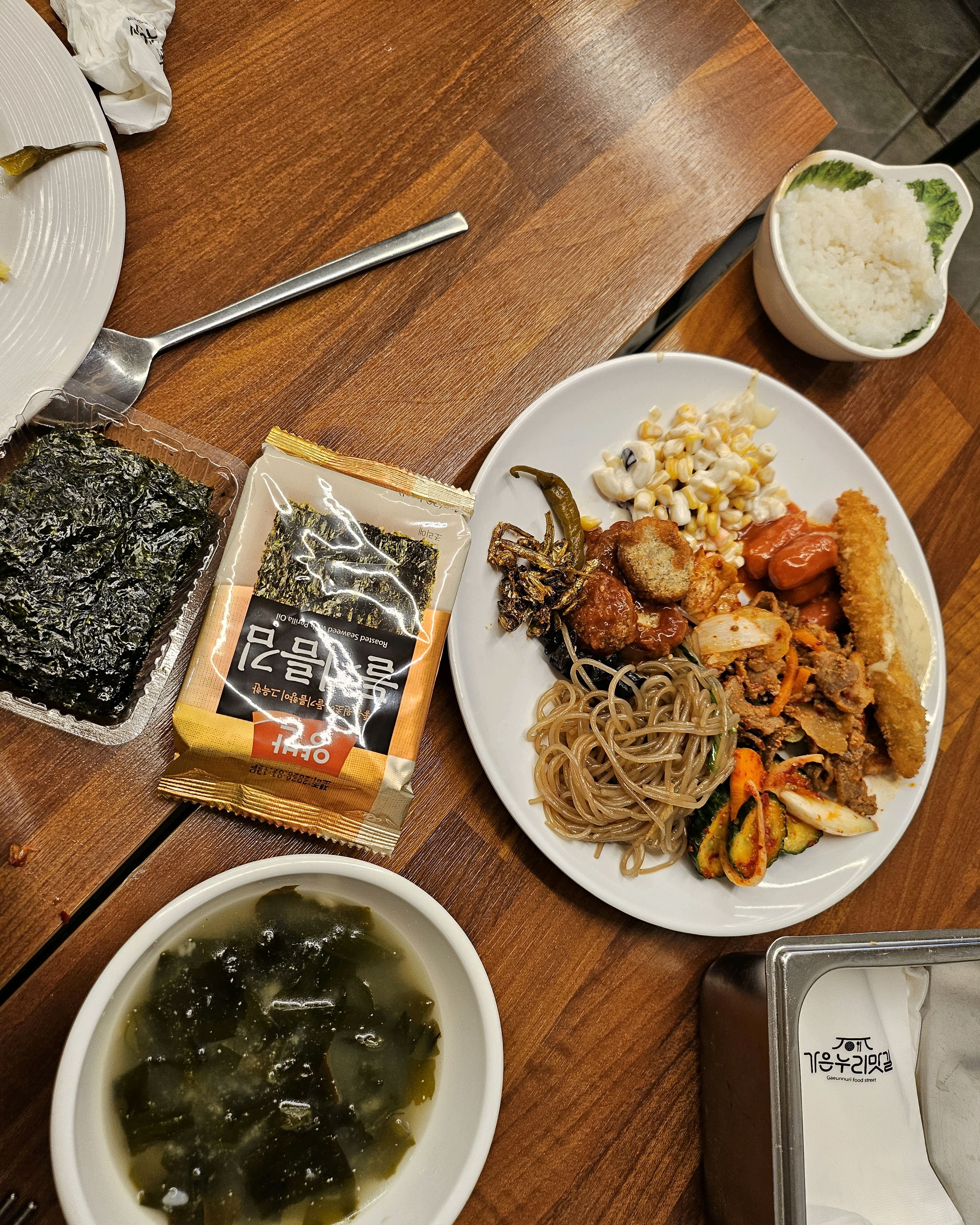 다양한 반찬들이 놓인 테이블 위에 김과 밥이 담긴 접시가 놓여 있는 모습