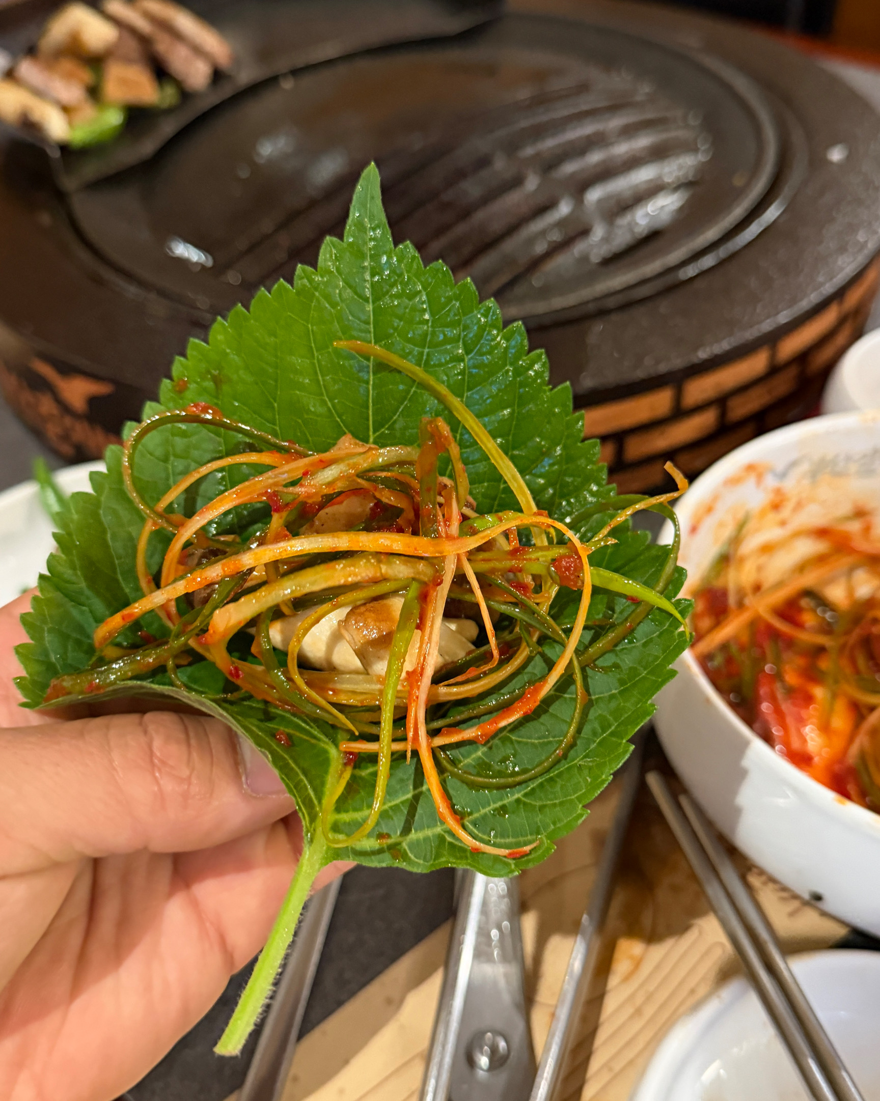 깻잎 위에 올라간 매콤하게 무쳐진 파채와 고기