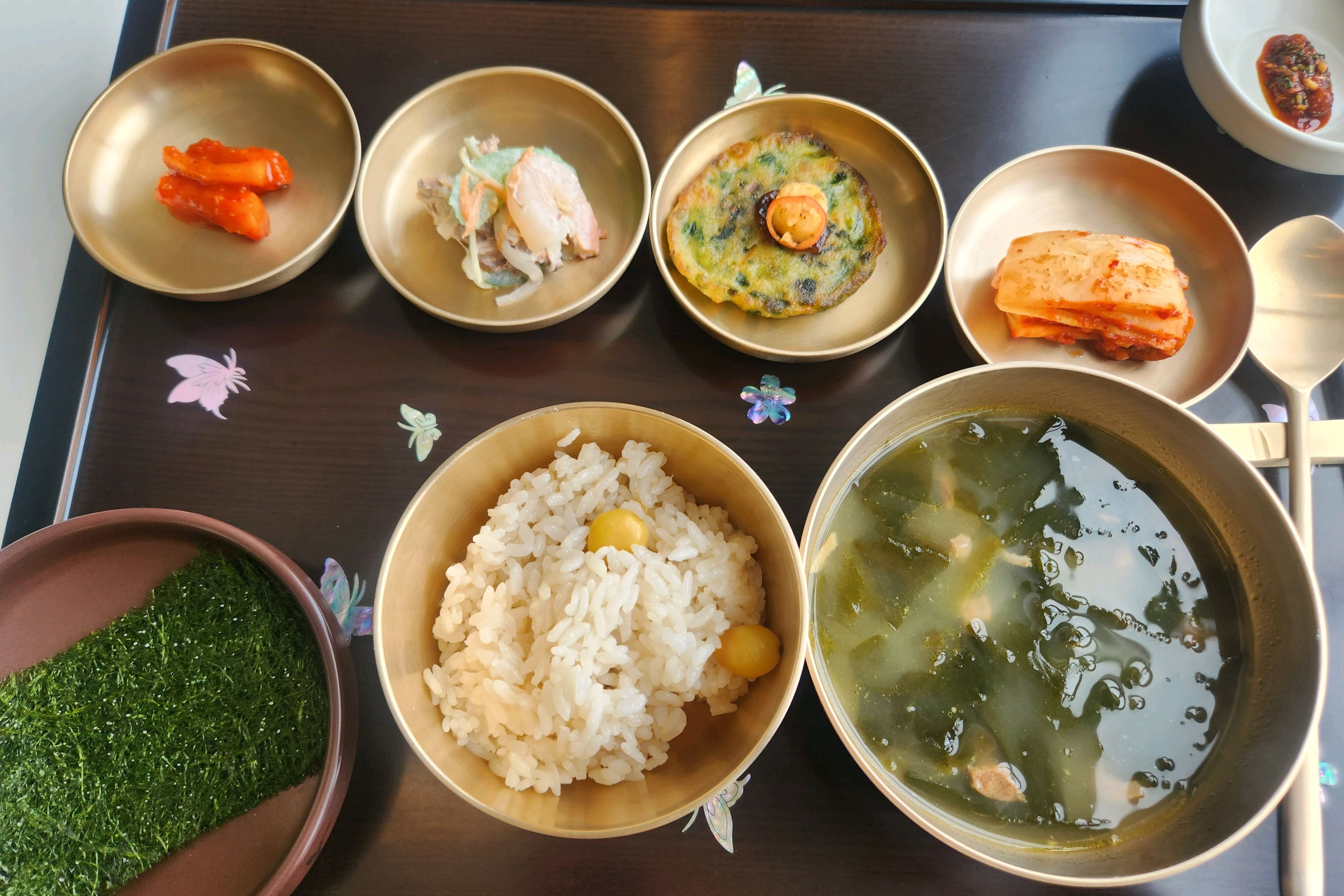 정갈하게 차려진 한 상 차림. 밥, 국, 그리고 여러 가지 반찬들이 놋그릇에 담겨 있다.