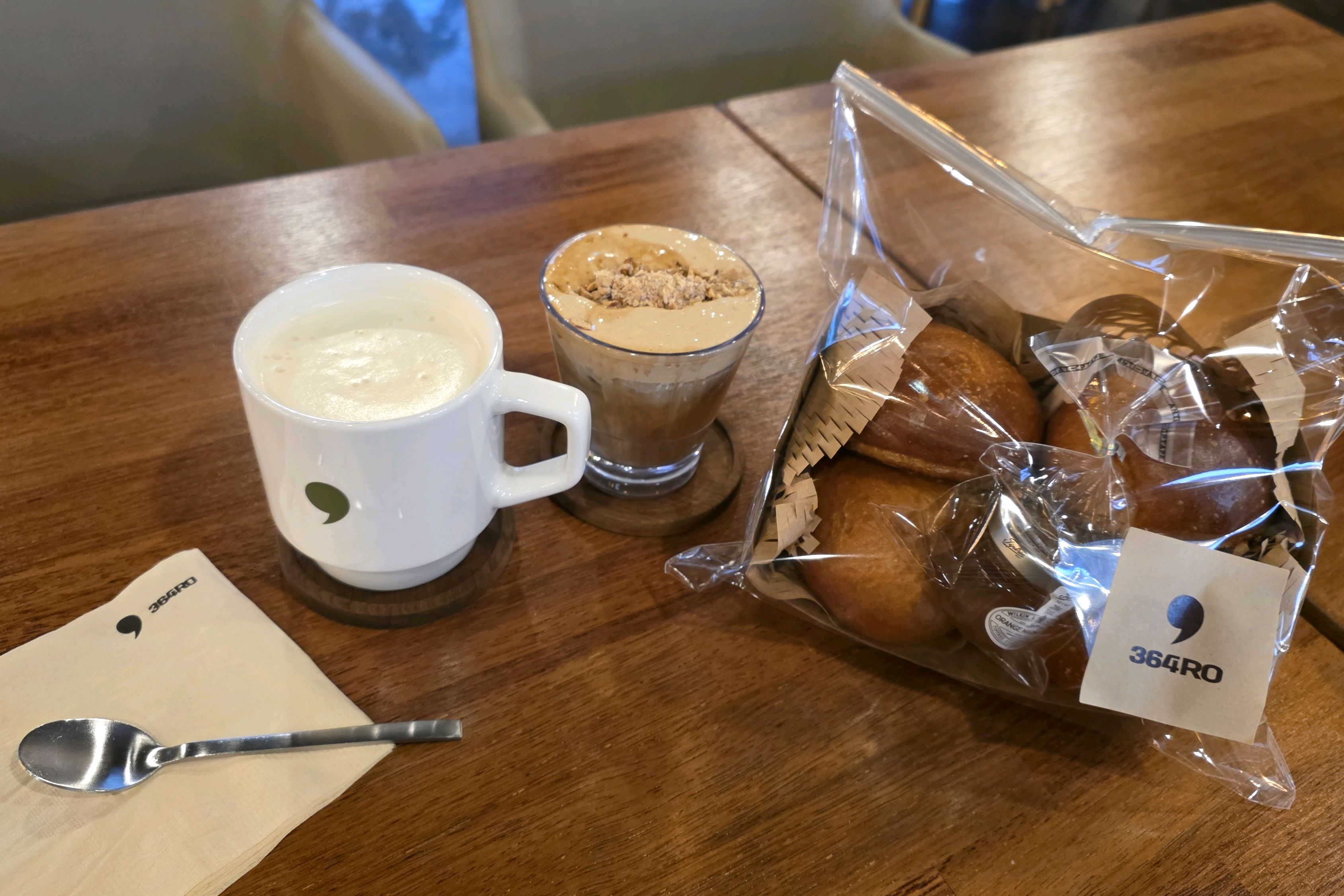 흰색 머그잔과 디저트 잔에 담긴 음료. 빵 봉투도 함께 놓여 있다.