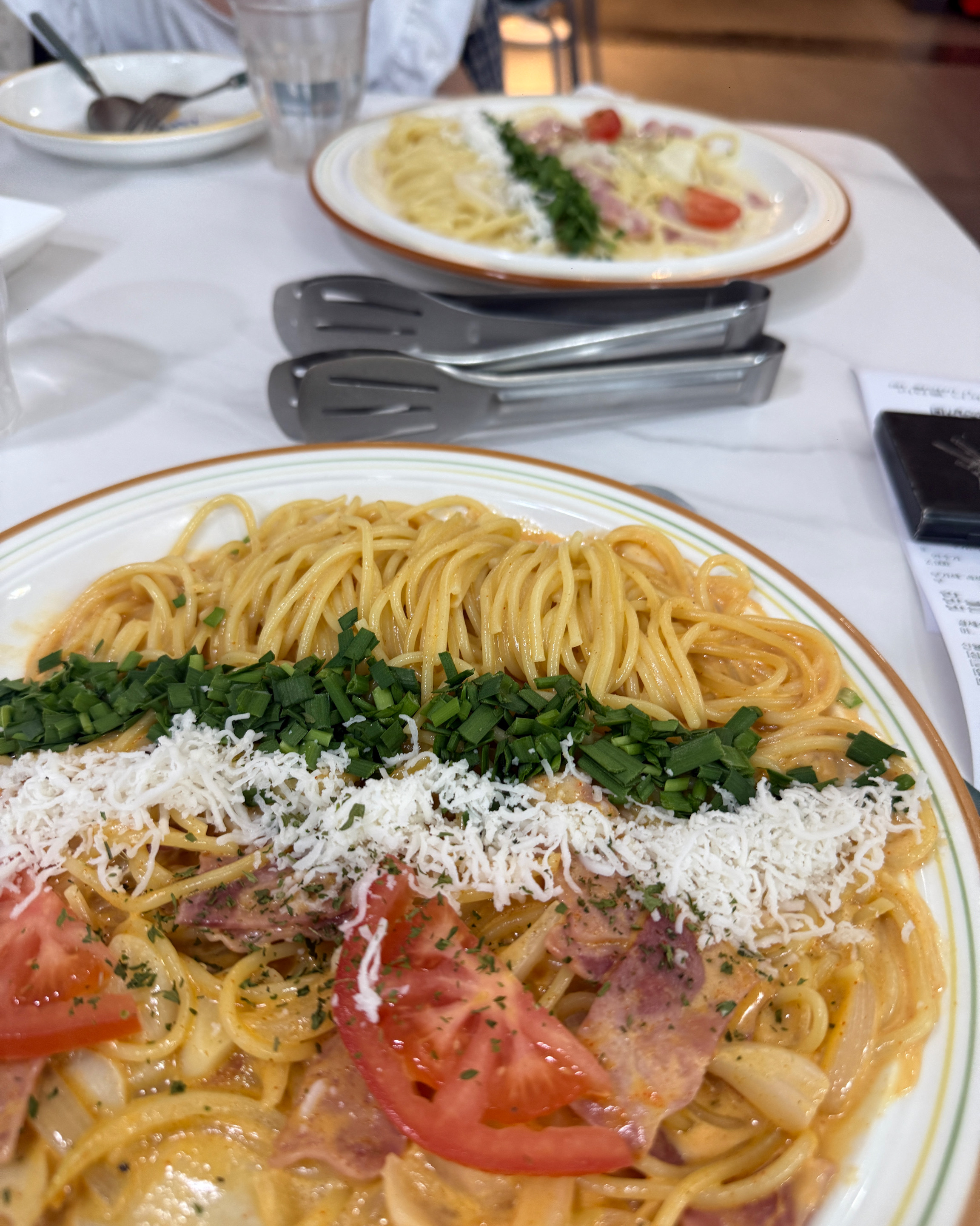 테이블 위에 놓인 두 개의 파스타 접시, 한쪽에는 치즈가 뿌려져 있습니다.