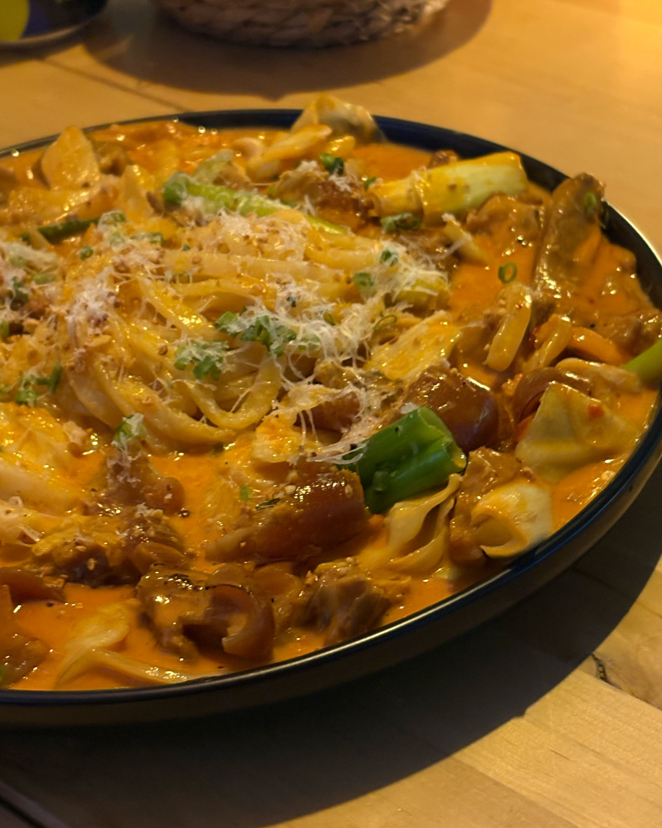 치즈 가루와 파가 뿌려진 로제 소스의 칼국수 볶음 요리가 접시에 담겨 있습니다.