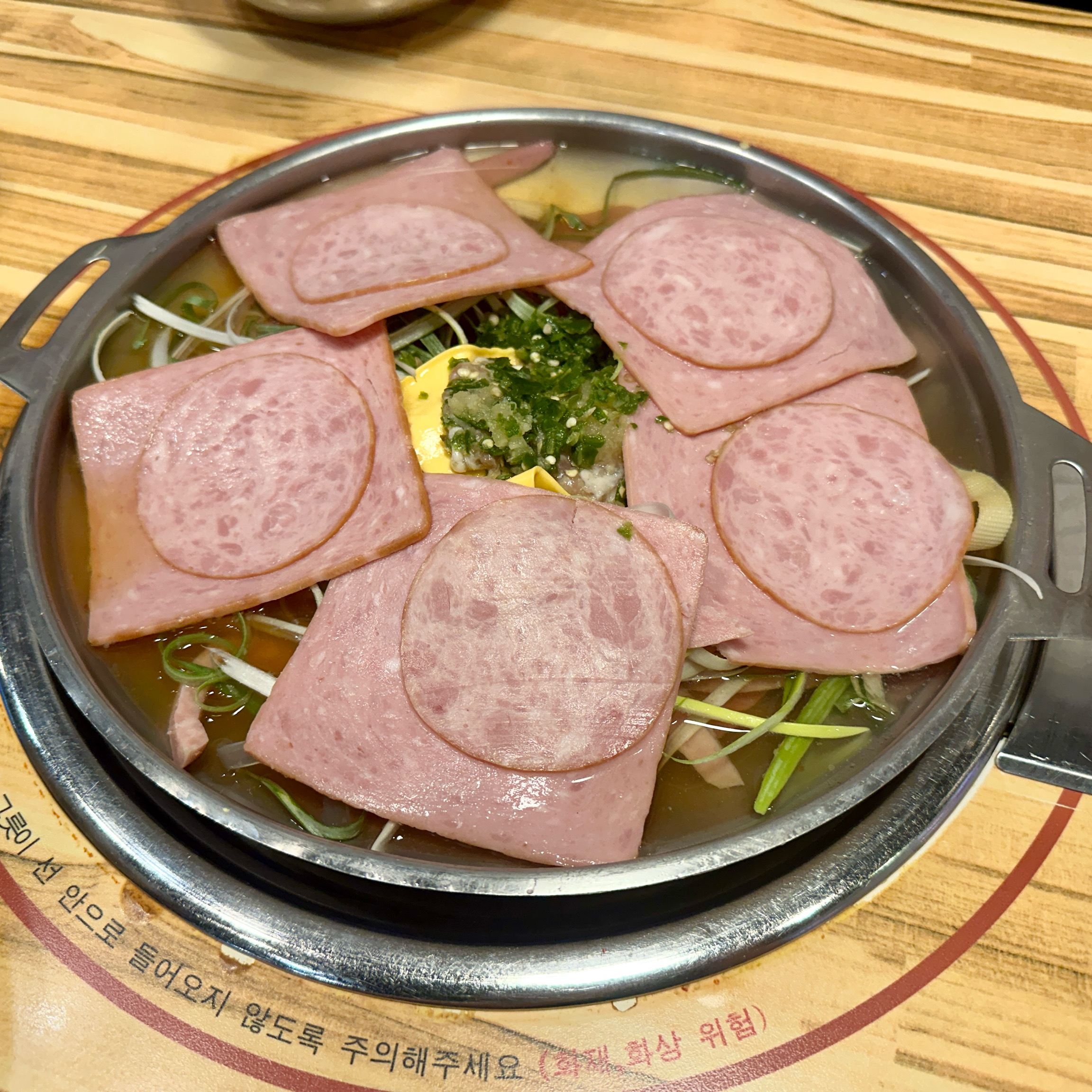 원형 전골 냄비에 얇은 햄과 치즈, 다진 양념이 올려진 부대전골