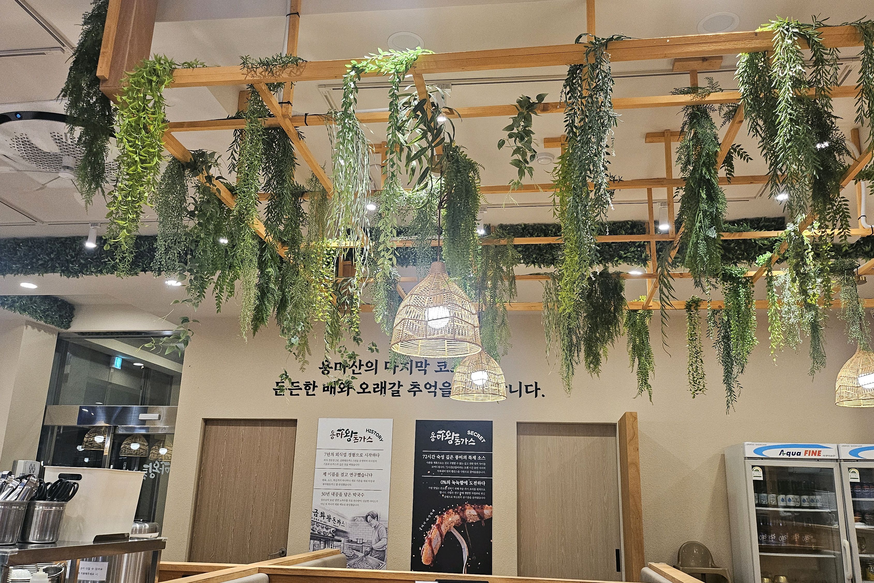 천장에 매달린 초록 식물과 라탄 조명, 용마산의 마지막 코스 문구가 적힌 용마왕돈까스 본점 홀