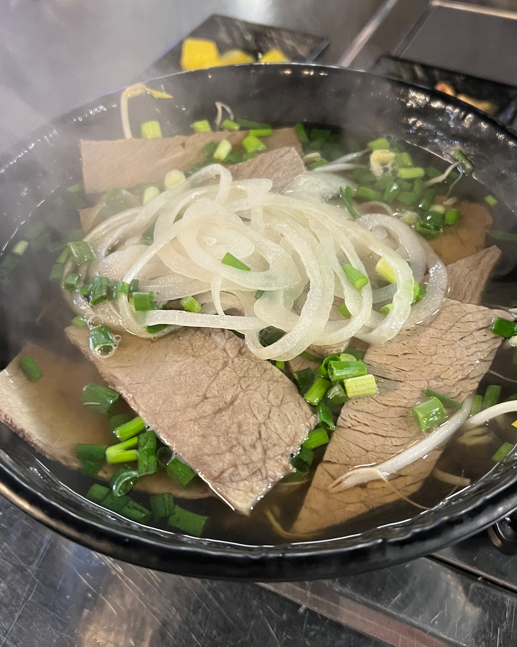 검은 그릇에 맑은 국물과 고기 편육, 양파, 파가 올려진 쌀국수
