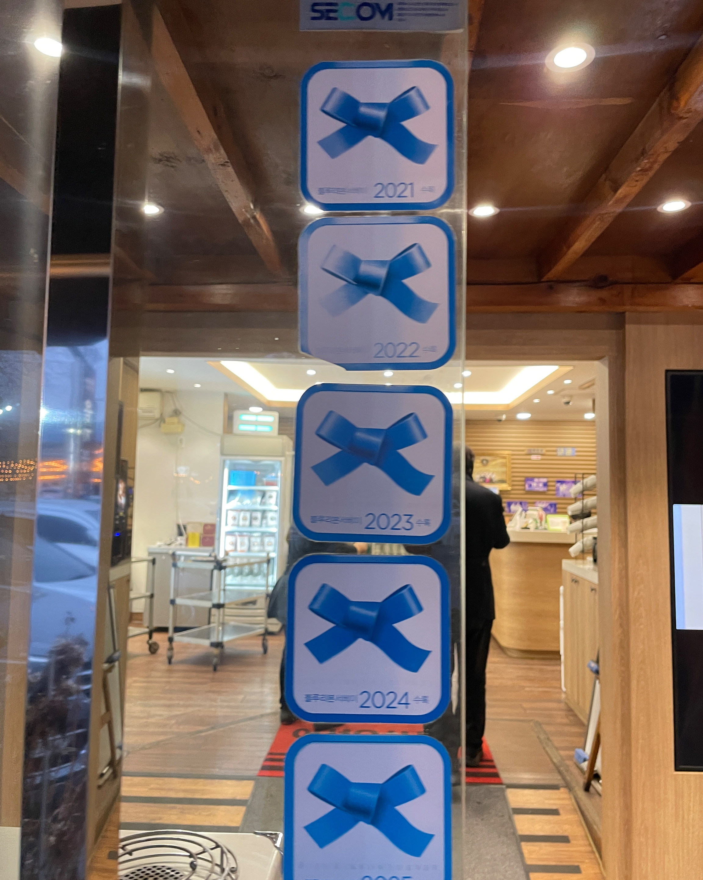 유리문에 여러 개의 푸른색 리본 모양 스티커가 연도별로 붙어 있다. 2021년부터 2025년까지 순서대로 나열되어 있다.
