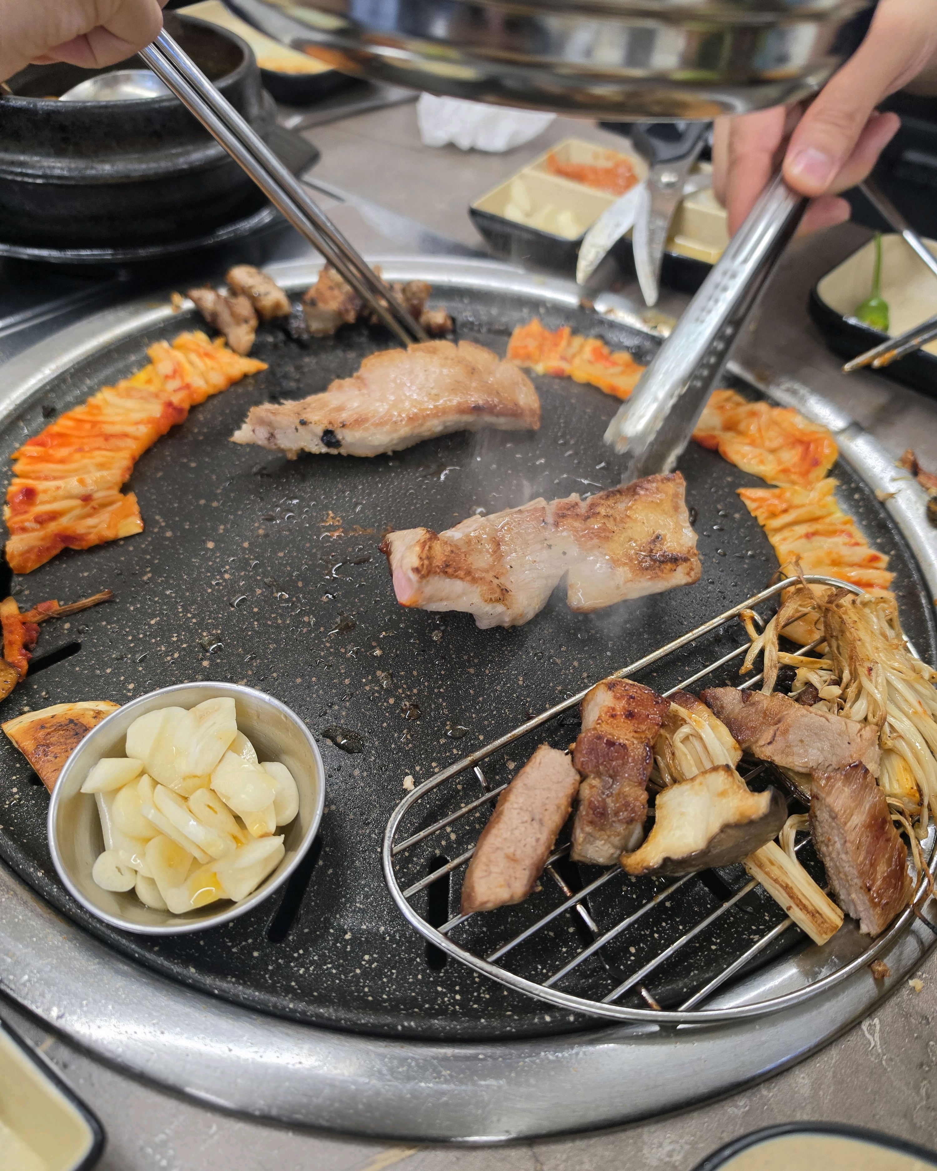 불판 위에서 익어가고 있는 고기와 김치, 곁들임 음식들